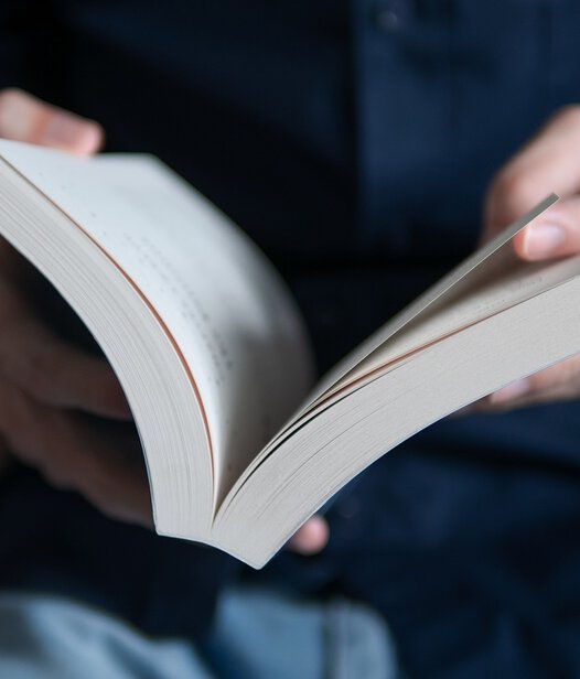 Mit Lehr- und Lernbüchern die IHK-Prüfung zur beschleunigten Grundqualfikation bestehen Nahaufnahme von Mann mit blauem Hemd blättert in weißem Buch